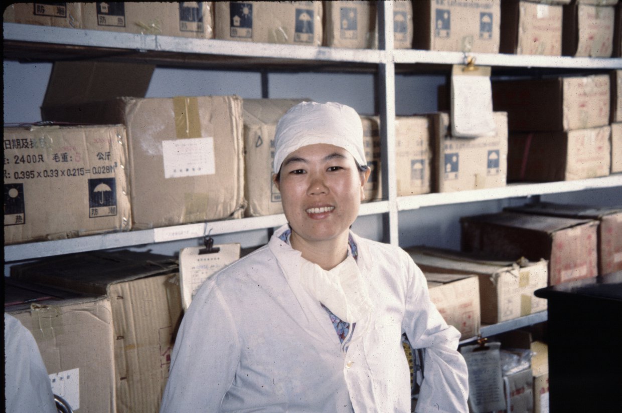 Woman wearing laboratory coat standing in front of shelves full of boxes.