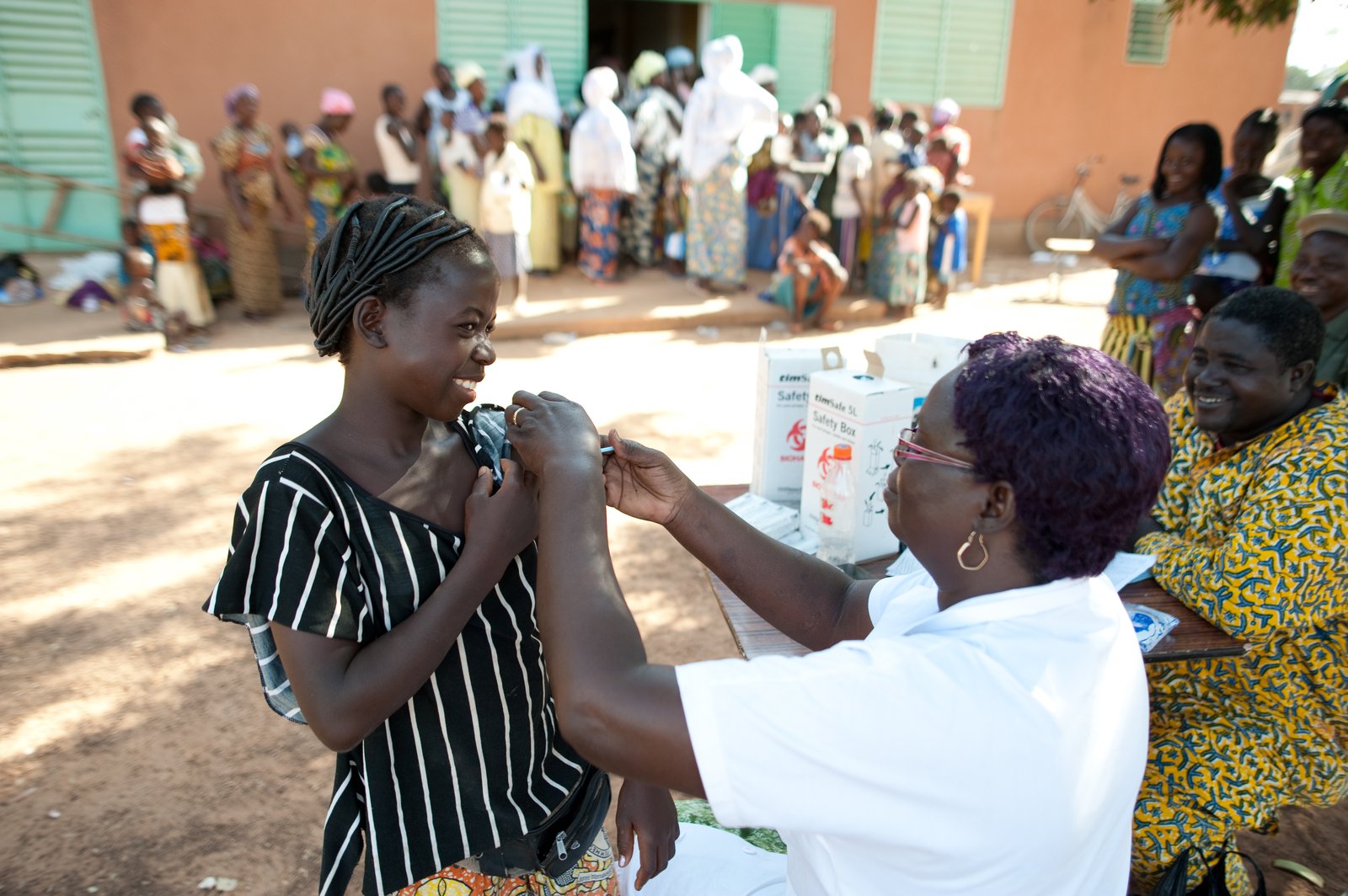 Young woman smiles as she recieves a shot in her upper arm from a health worker.
