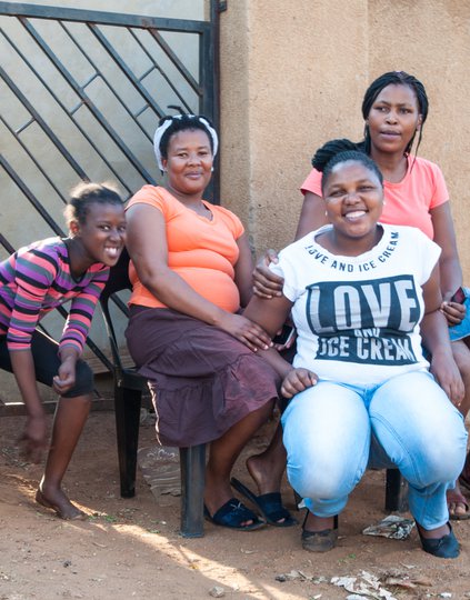 A girl and three women sitting by a wall.