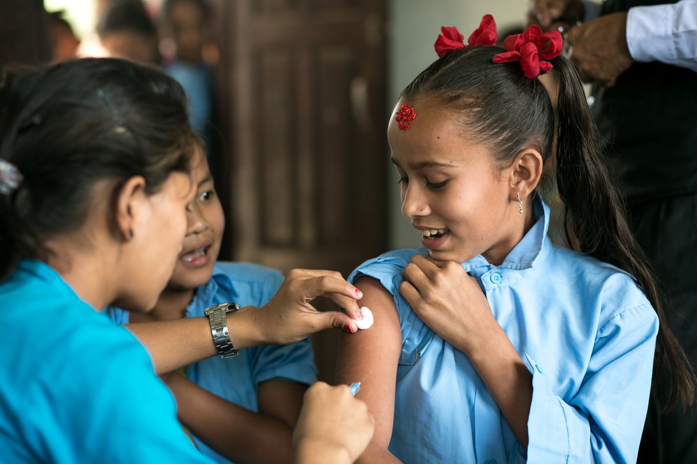 A woman gives a girl an injection as others wait behind her.