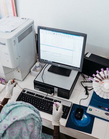 Laboratory technician placing vials of blood in a centrifuge machine and logging information in the computer in the regional hospital laboratory in Thies, Senegal. Photo: PATH/Gabe Bienczycki.