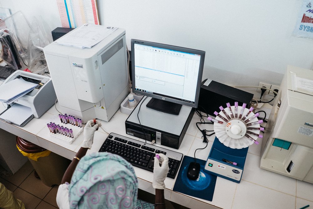 Laboratory technician placing vials of blood in a centrifuge machine and logging information in the computer in the regional hospital laboratory in Thies, Senegal. Photo: PATH/Gabe Bienczycki.