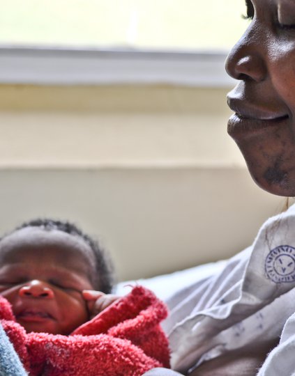 A smiling mother holds a newborn wrapped in a red blanket.