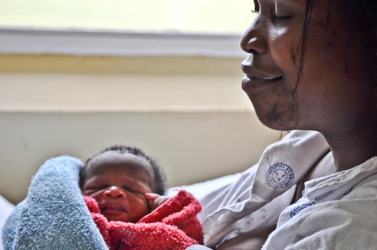 A smiling mother holds a newborn wrapped in a red blanket.