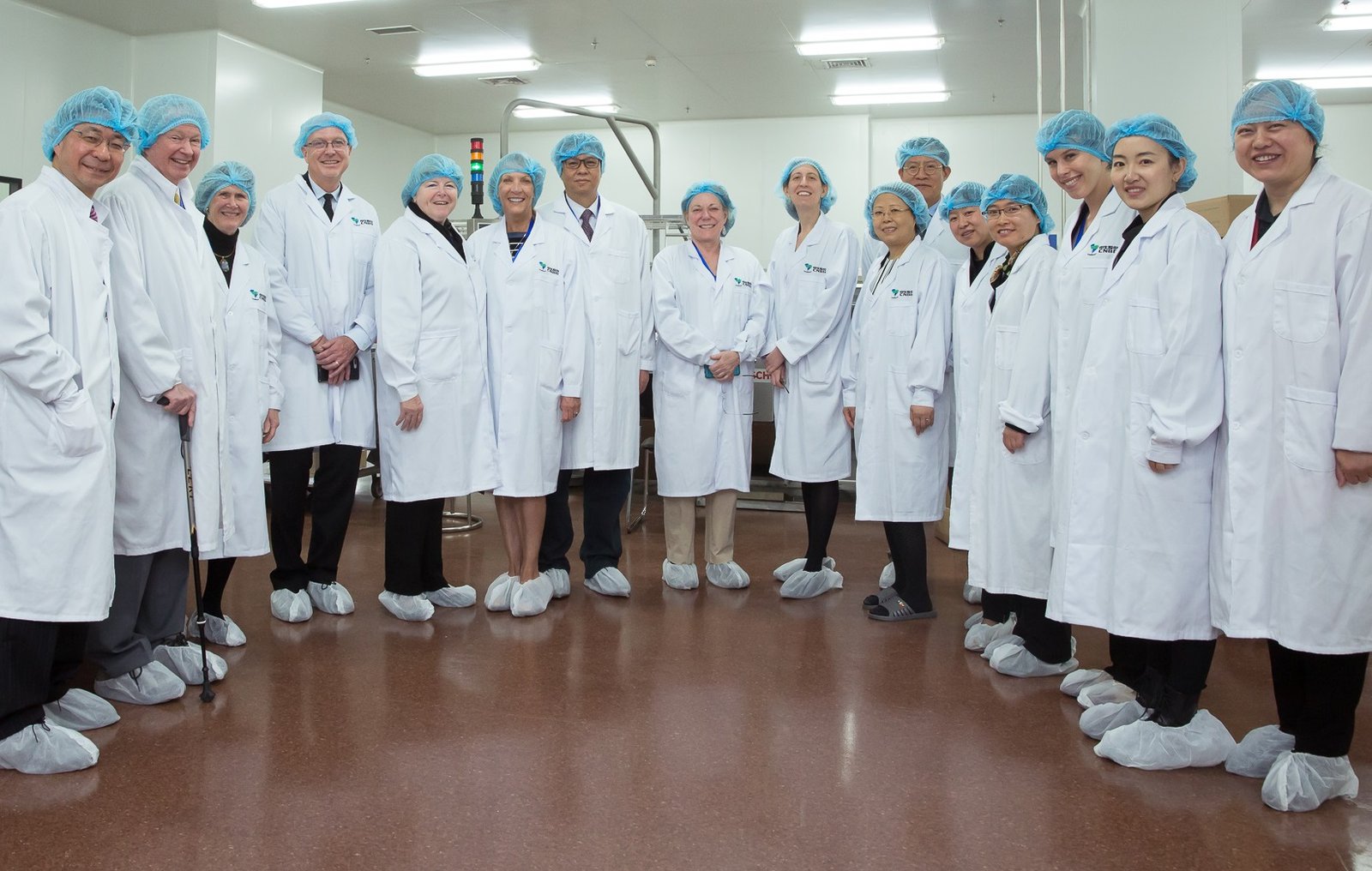 PATH Journeys travelers in China dressed in lab coats and hairnets standing in a semicircle smiling at the camera.