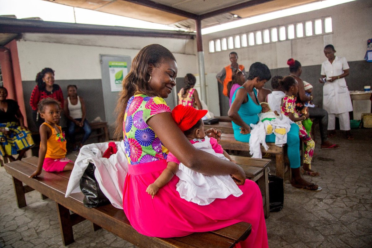 A woman cradles a toddler in her lap in a waiting room at a clinic.
