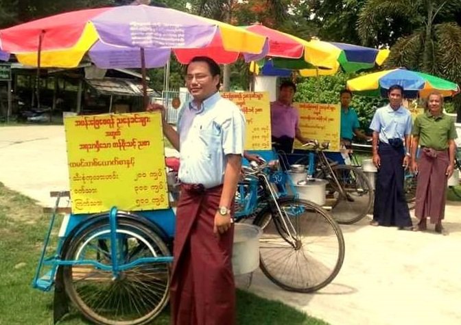 Several men stand in line with bicycles and umbrellas.