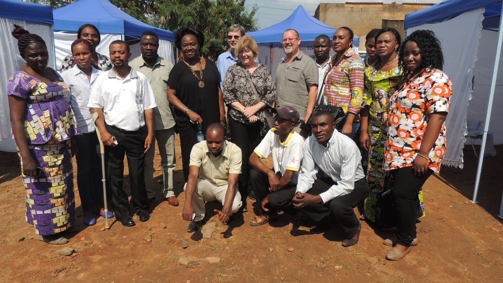 A group of people stand between tents, flanking Kathy Cahill and David Fleming.