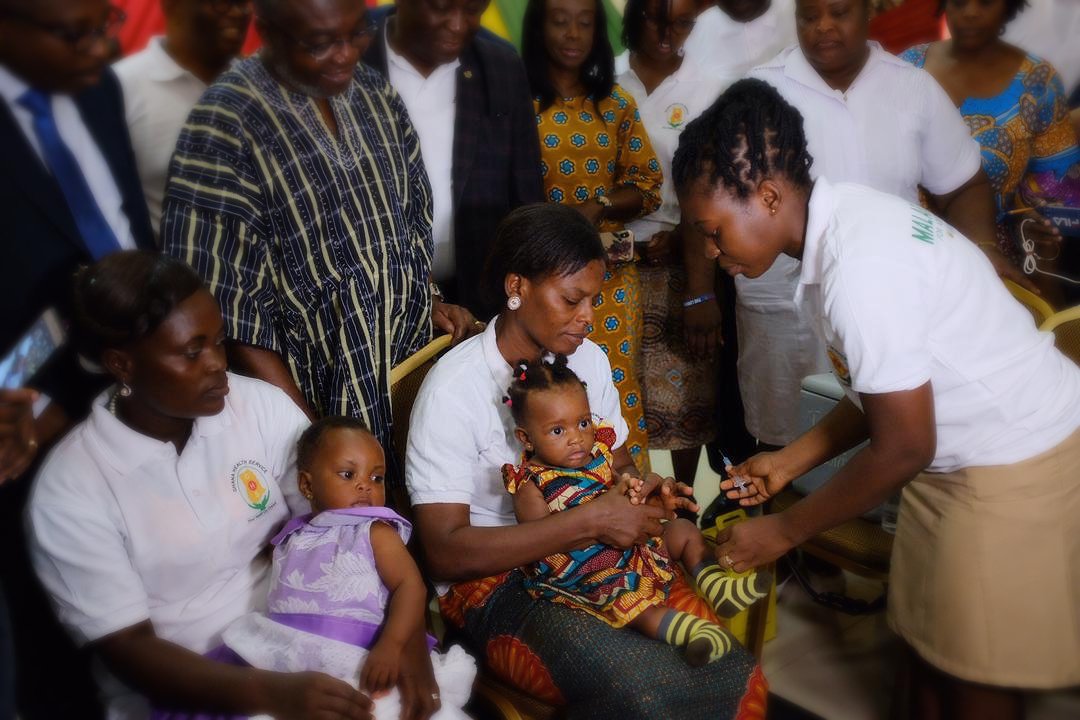 Two mothers give their 6-month-old babies Akwanyi and Susana the new malaria vaccine during the national launch of the Ghana Malaria Vaccine Implementation Program.