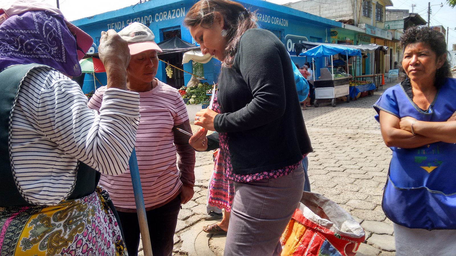 A woman holding a device talks to two other women while a third woman looks on.
