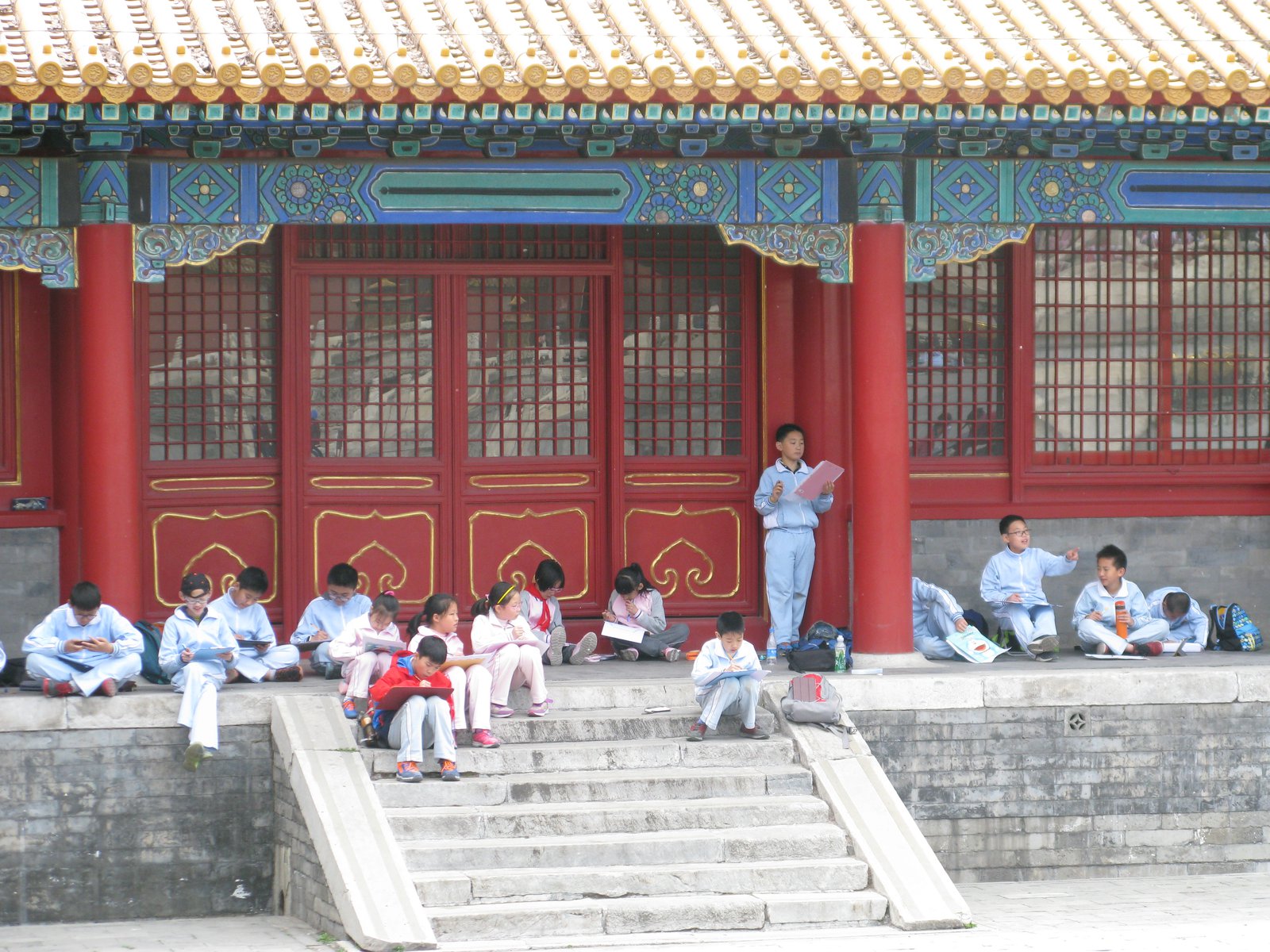 Children seated together on steps outside a building in the Forbidden City.