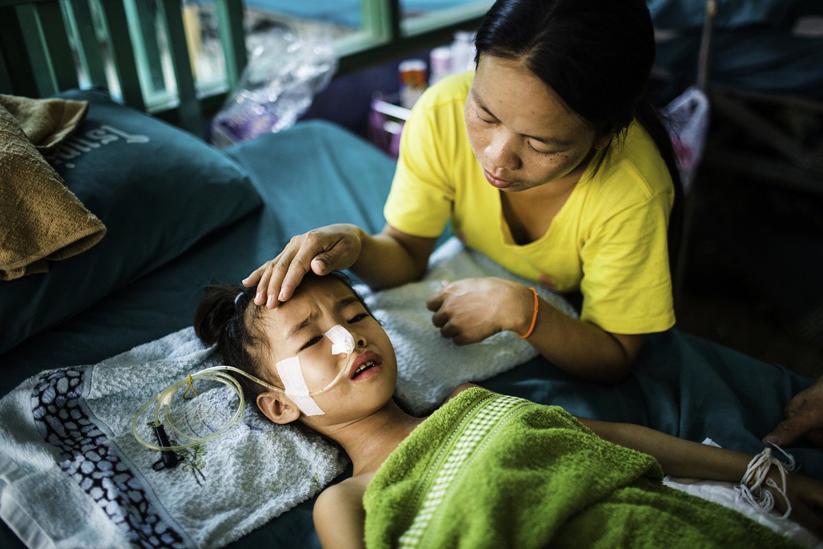 Girl in hospital bed with tube up her nose and mother comforting her.