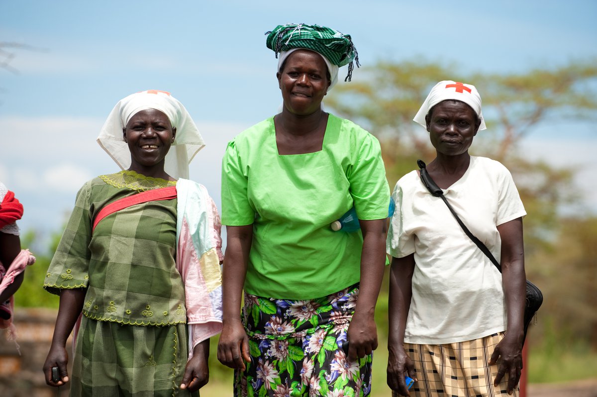 Three women wearing head scarves with red cross insignia and smiling.