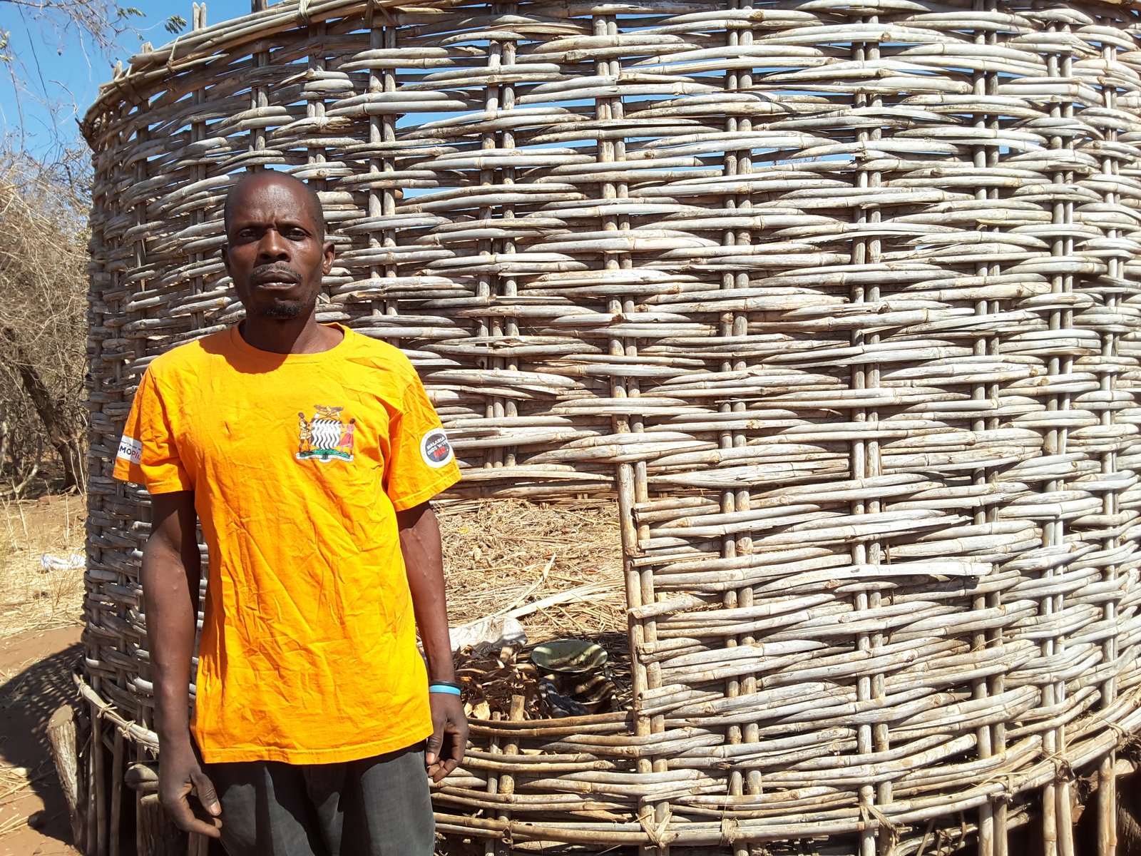 Masauso Mbewe, a 42-year-old community health worker from Lusangazi District, stands next to his empty maize storage bin. Photo: PATH.