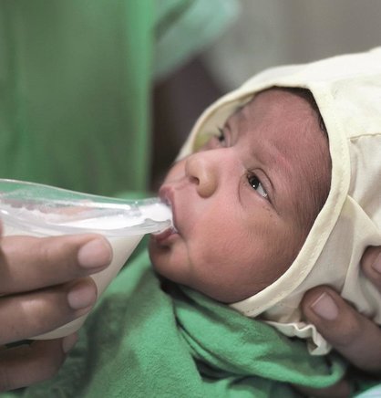 An infant sips human milk from the Nifty Feeding Cup.