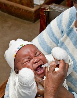 A crying baby in its mother's arms is given a dose of oral vaccine.